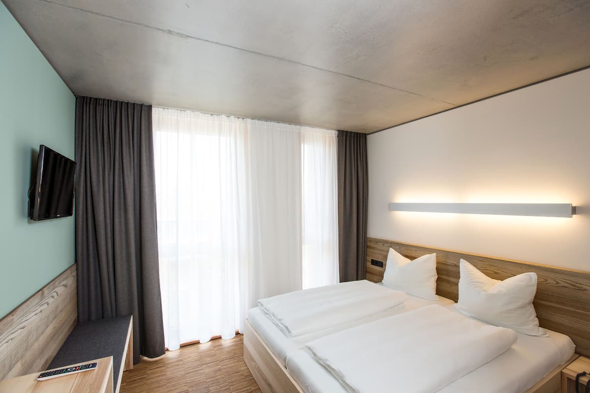 A hotel room with a bed, a TV mounted on the wall, and a bedside table.