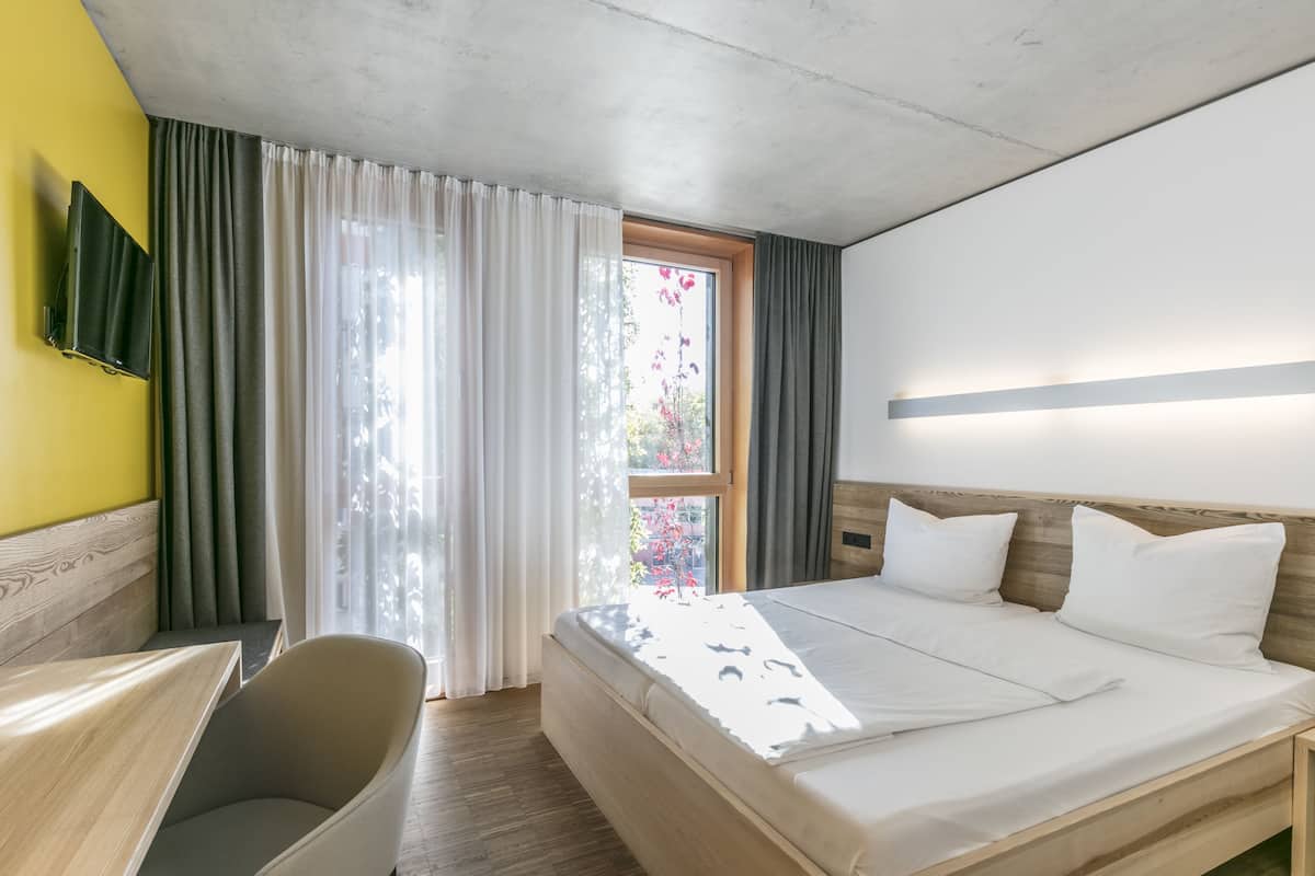 A hotel room with a bed, a desk, and a TV mounted on the wall.