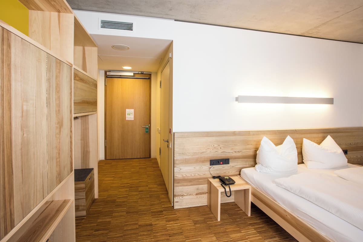 A hotel room with a wooden floor, a bed with white bedding, a bedside table with a phone, and a wooden wardrobe.