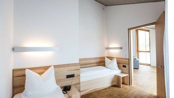 Ein modernes Hotelzimmer mit zwei Betten, Holz-Kopfteilen, Nachttischen und einem großen Fenster, das natürliches Licht hereinlässt.