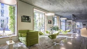 Un interior moderno con un sofá verde, sillas verdes y ventanas amplias que ofrecen vistas a zonas verdes y edificios.