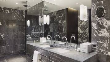 A modern bathroom with marble walls, a large mirror, dual sinks, and a towel rack.