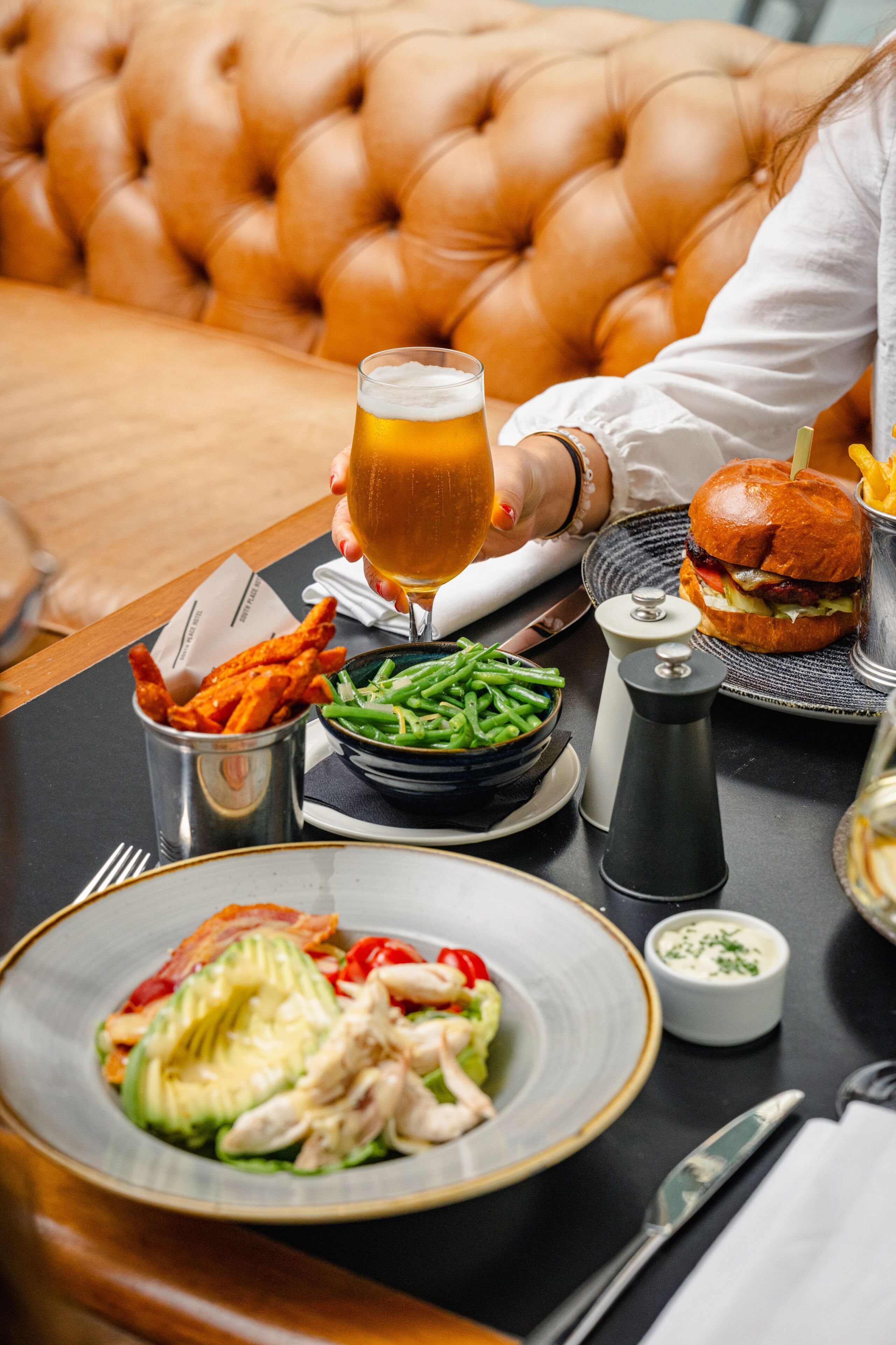 A dining table with a meal, a glass of beer, and a burger.