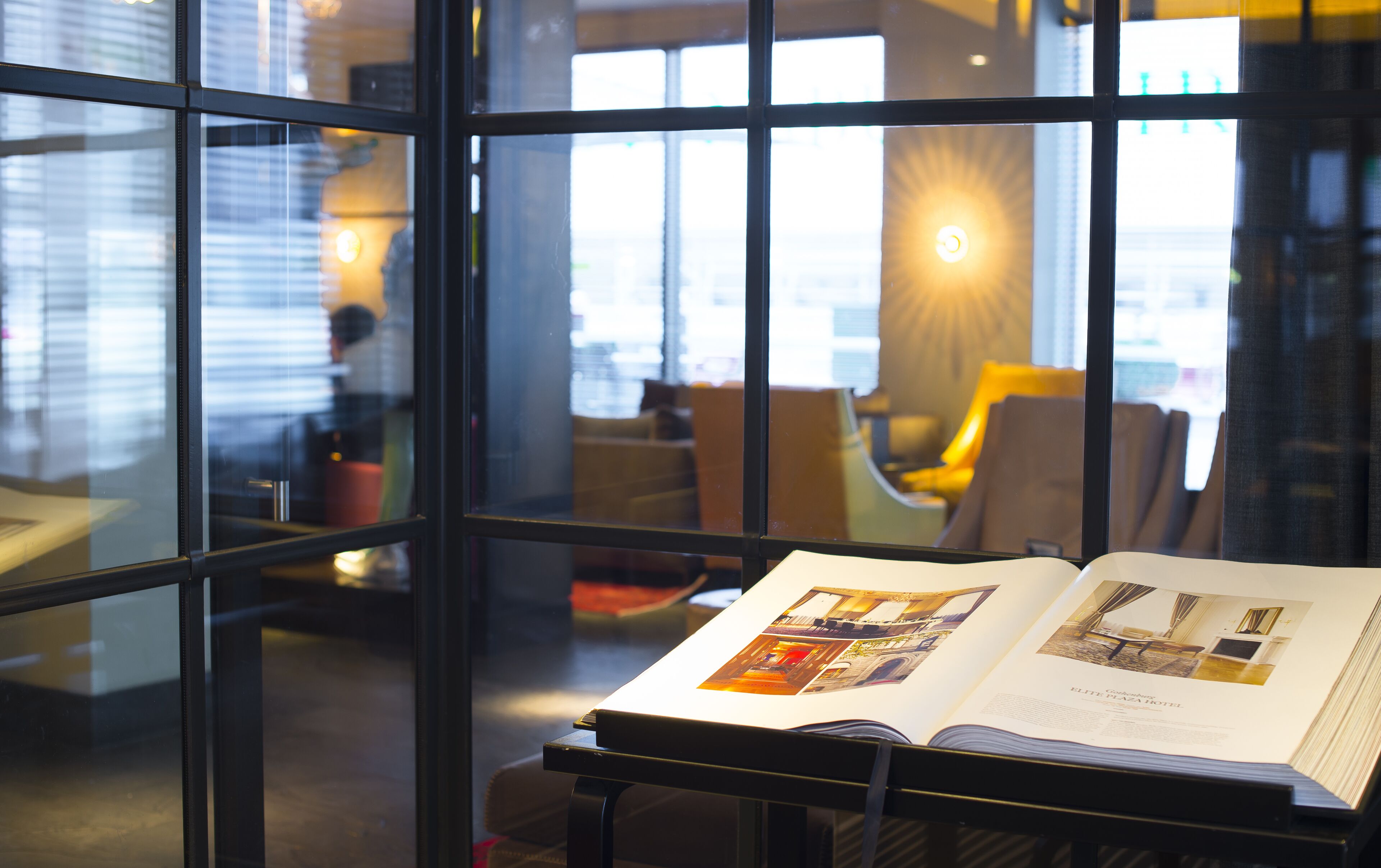 An open magazine on a table in a well-lit room with large windows, modern furniture, and a view of the cityscape.