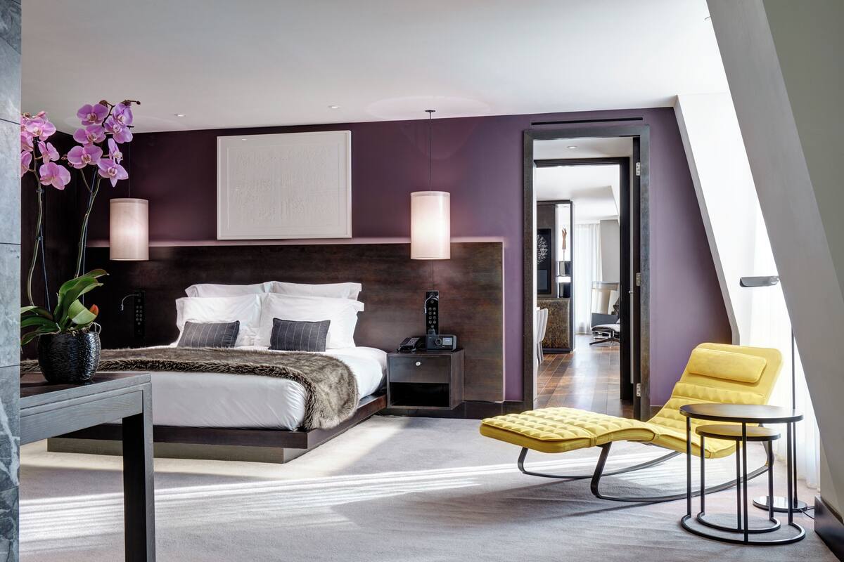 A modern bedroom with a bed, bedside table, lamp, and a yellow chair.