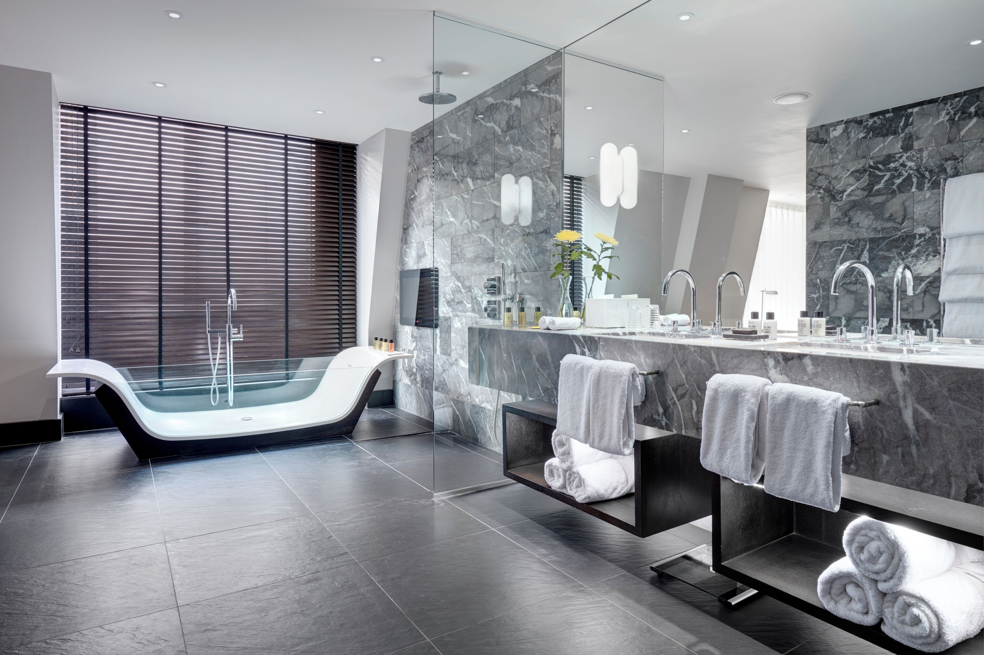 A modern bathroom with a freestanding bathtub, a large mirror, and a marble backsplash.