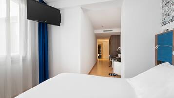 Una camera d'albergo con un letto, una TV a parete, un bagno con specchio e un corridoio che porta a un'altra stanza.