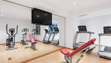 A gym with exercise equipment, a large mirror, and a TV on the wall.