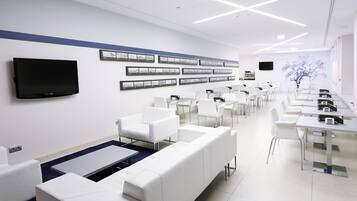 A modern conference room with white furniture, a flat-screen TV, and framed pictures on the wall.