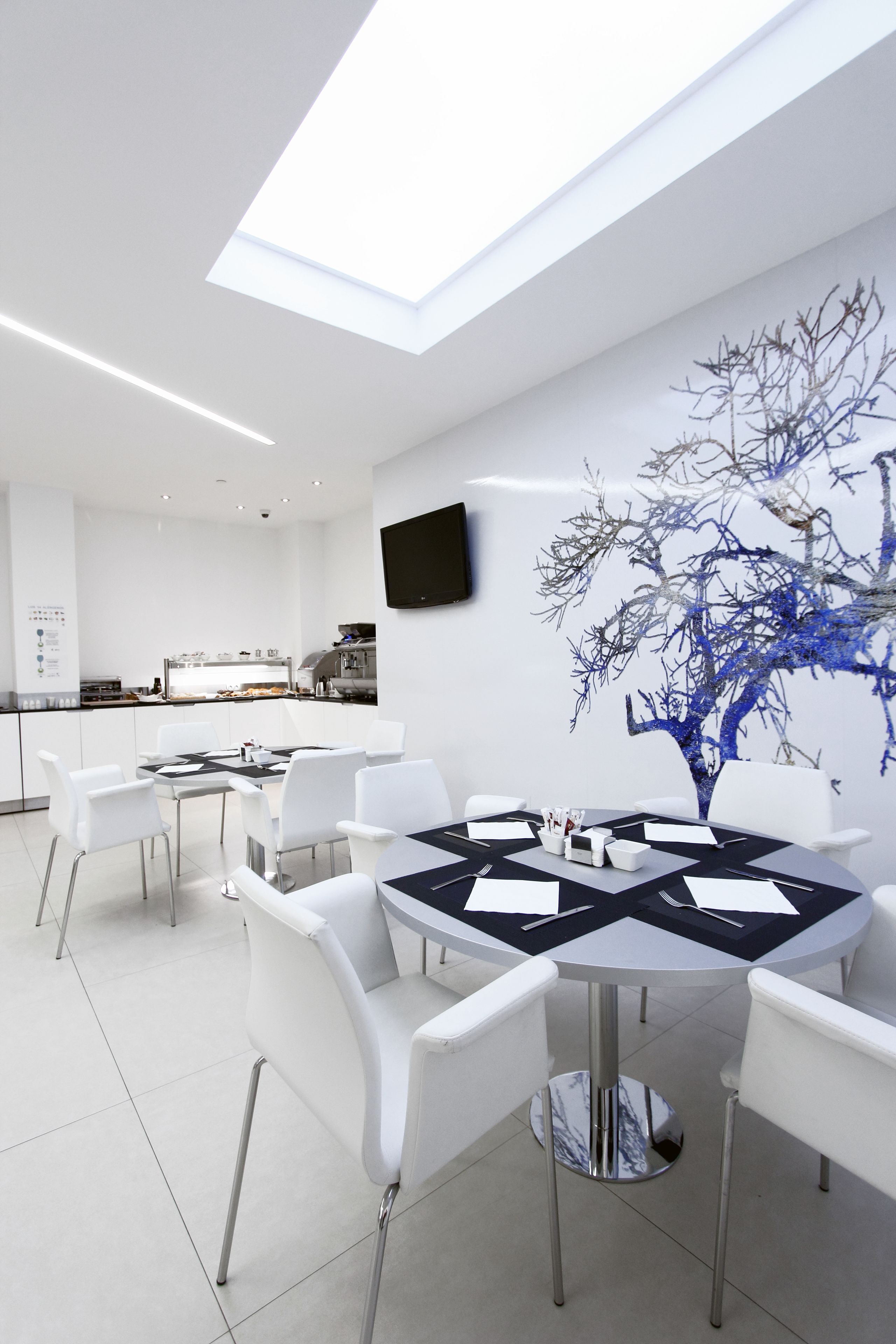 Una cocina moderna con armarios blancos, un comedor con una mesa redonda y sillas blancas, y un mural grande con un árbol en la pared.
