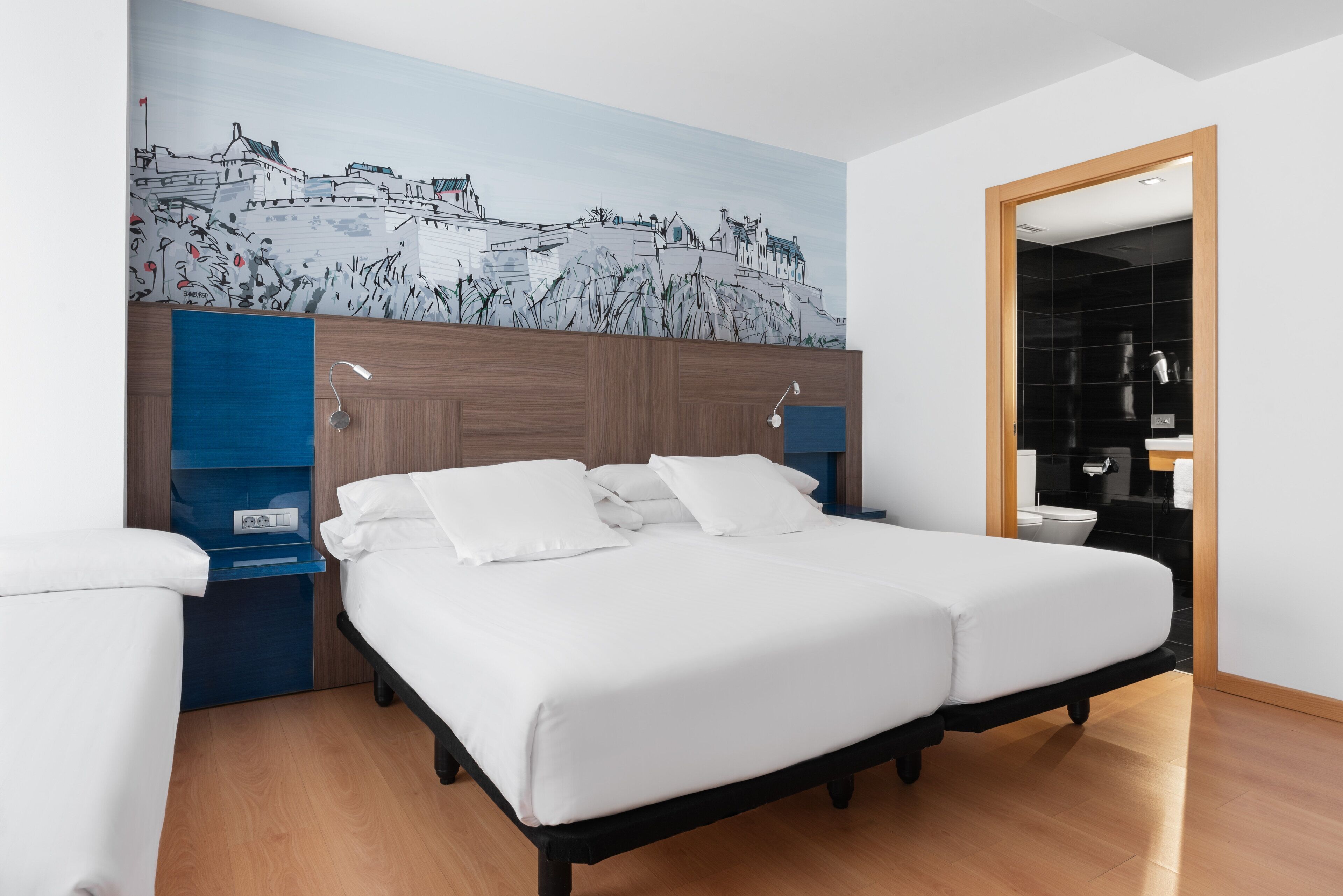 A double bed with white linens, a wooden headboard, and a cityscape mural on the wall.