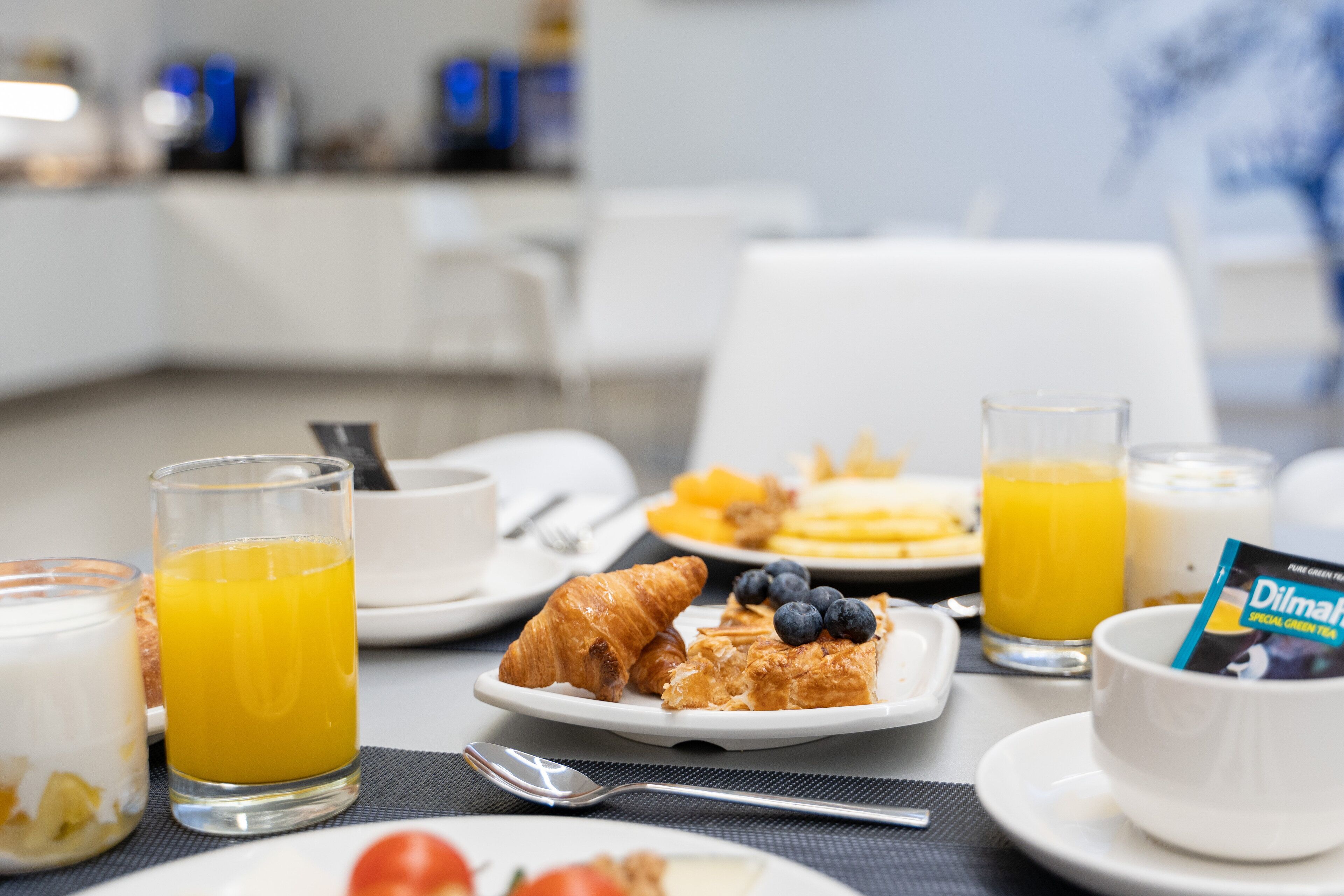 A breakfast setting with plates of food, glasses of orange juice, and a bowl of cereal.