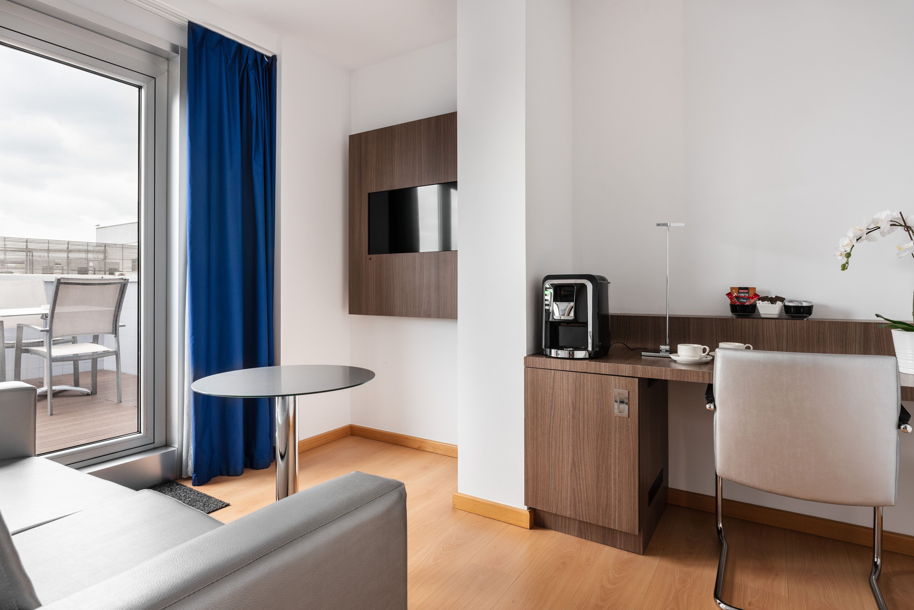 Una habitación de hotel moderna con zona de estar, una kitchenette pequeña y vistas a través de un ventanal grande.