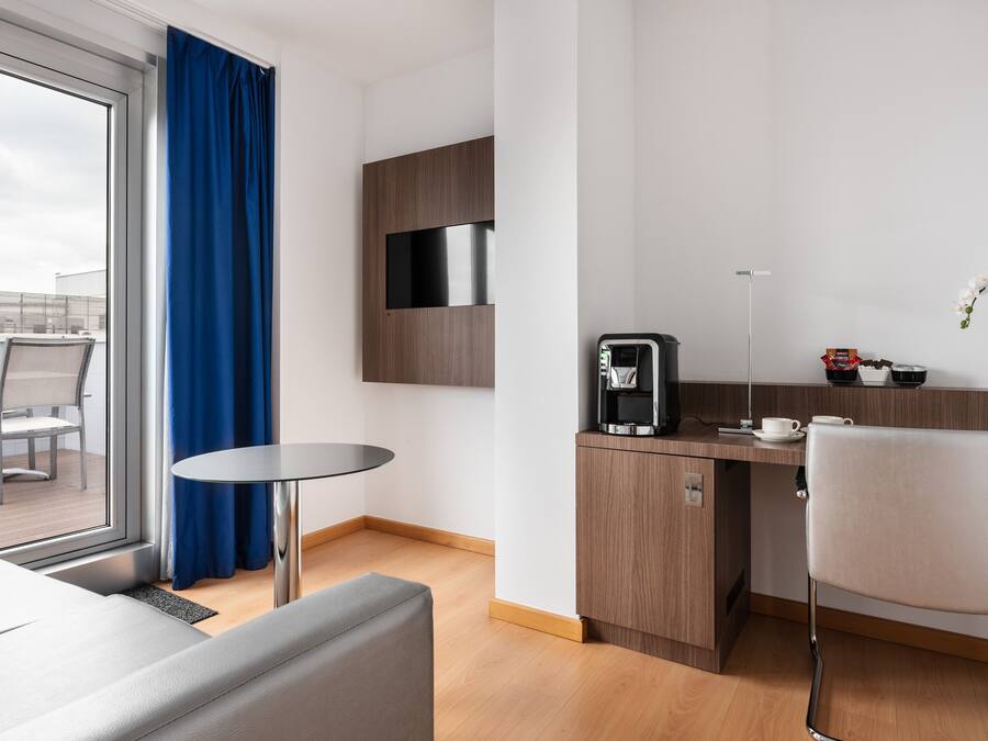 Una habitación de hotel moderna con zona de estar, una kitchenette pequeña y vistas a través de un ventanal grande.