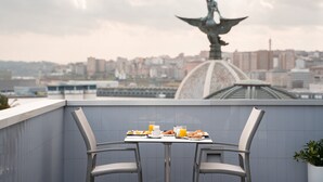 Un espace de restauration aménagé sur le toit, avec une table pour deux, offrant une vue sur le paysage urbain et une statue.