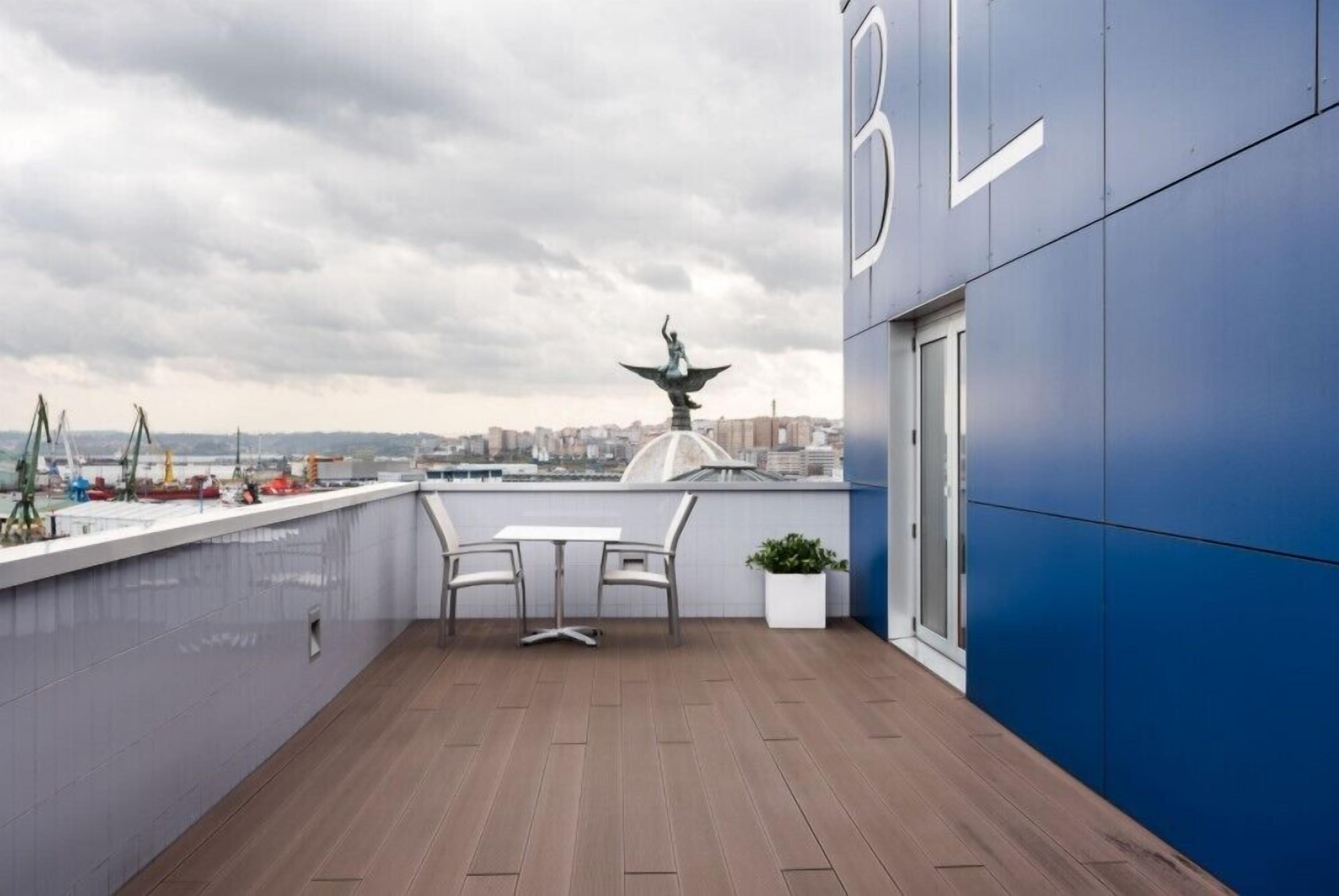 A rooftop terrace with a view of the city, a statue, and a table with chairs.
