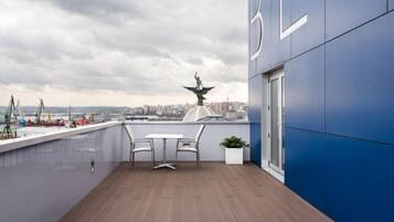 A rooftop terrace with a view of the city, a statue, and a table with chairs.