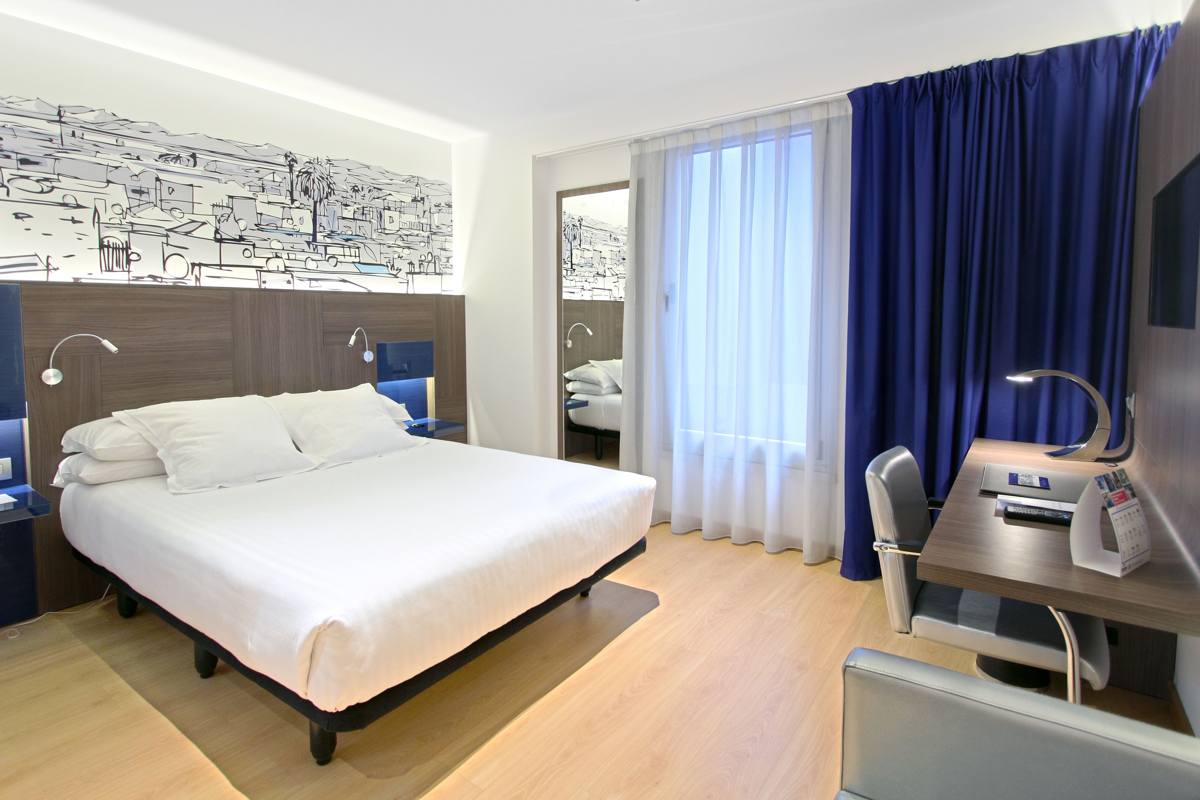 Habitación de hotel moderna con una cama grande, un escritorio con silla y vistas a la ciudad desde la ventana.