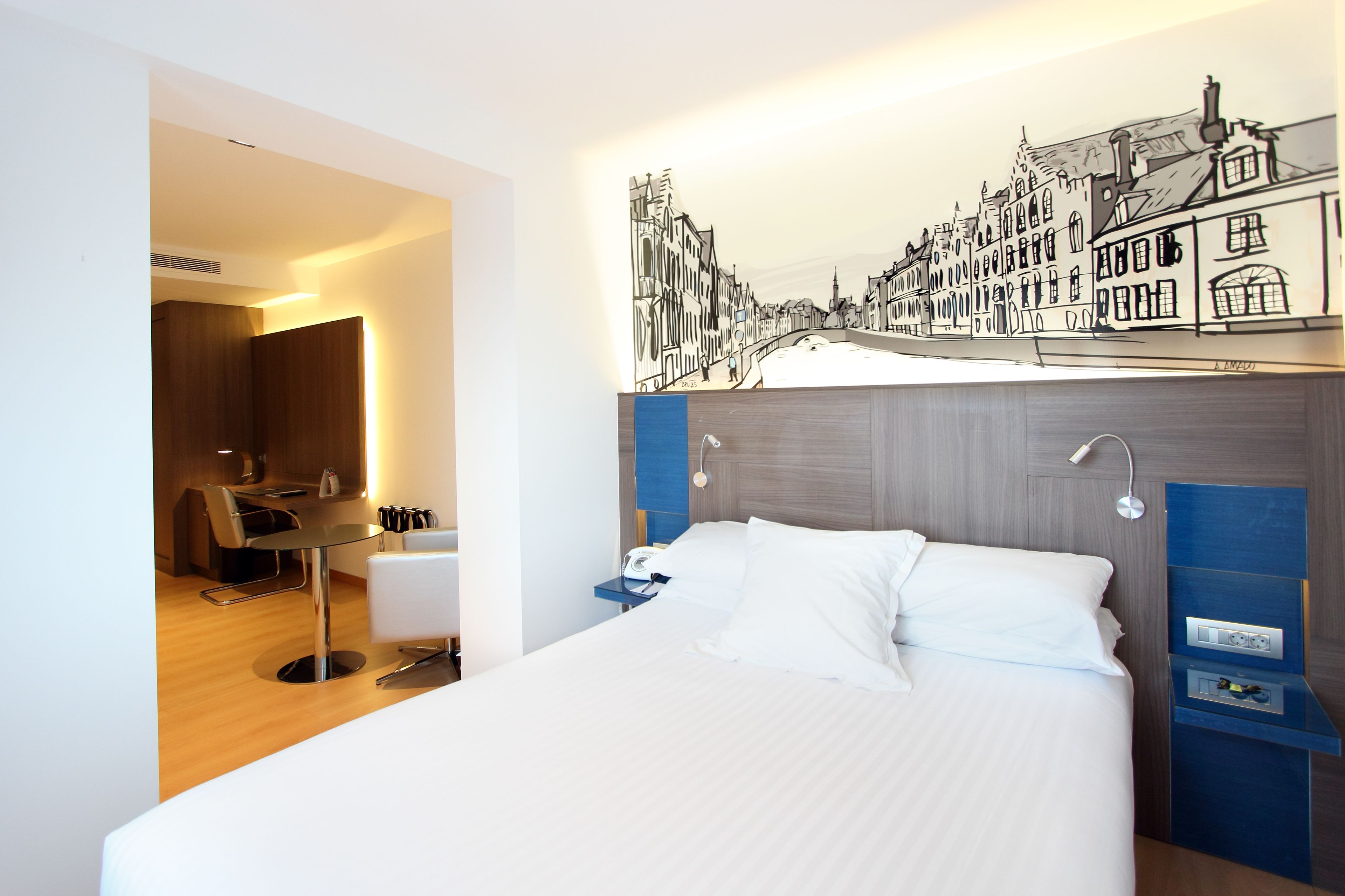 A hotel room with a bed, bedside tables, a desk, and a chair.