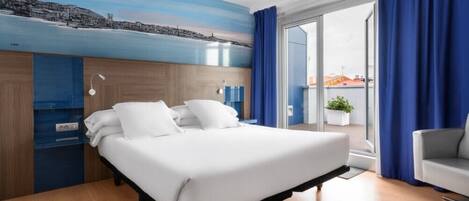 A modern hotel room with a large bed, a cityscape mural on the wall, a balcony with blue curtains, and a view of buildings outside.