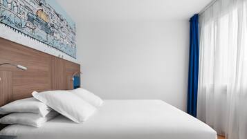 Una cama bien hecha con sábanas y almohadas blancas, un cabecero de madera y una lámpara de pared.