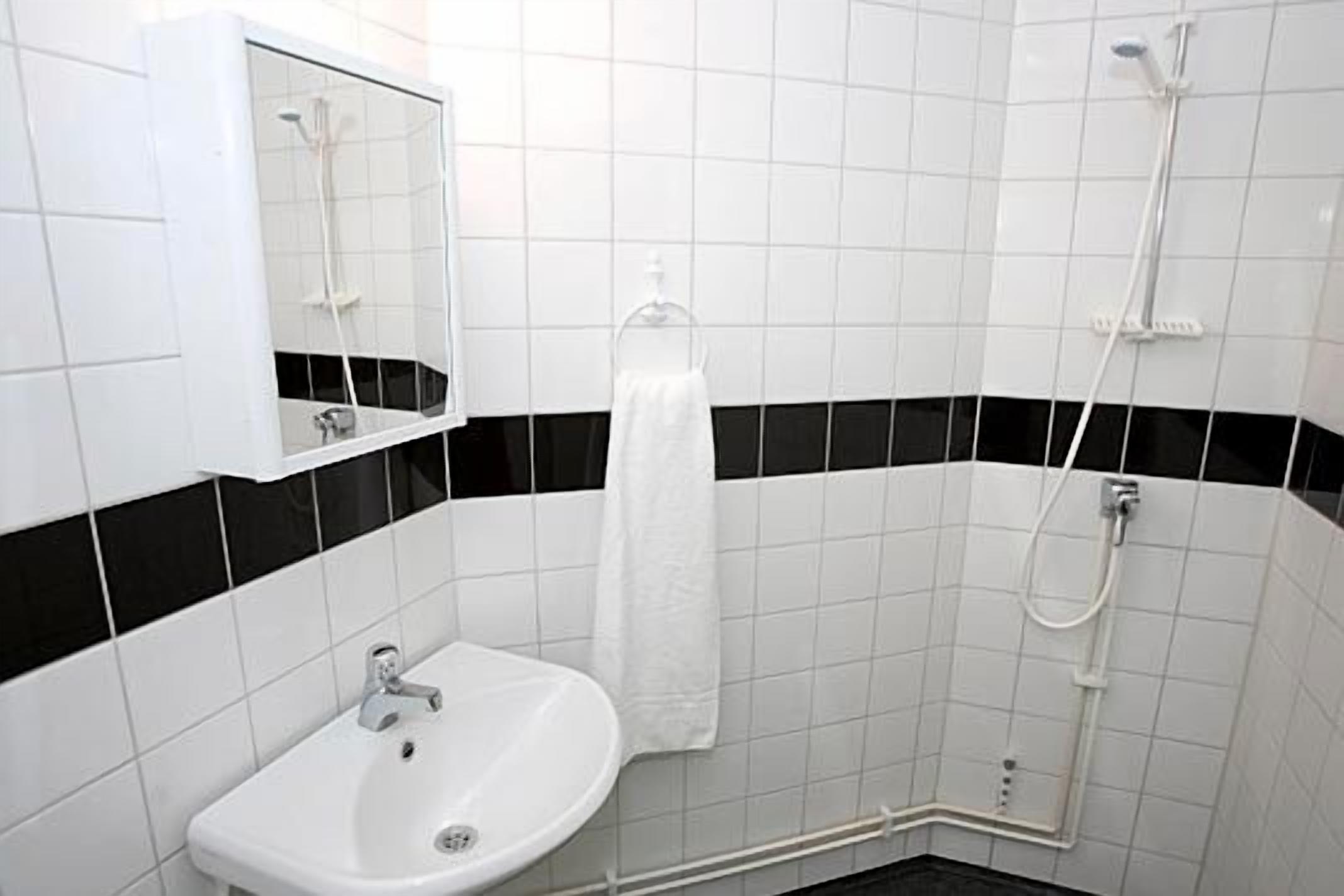 Un bany amb rajoles blanques, un lavabo, un mirall, un suport per tovalloles i una dutxa.