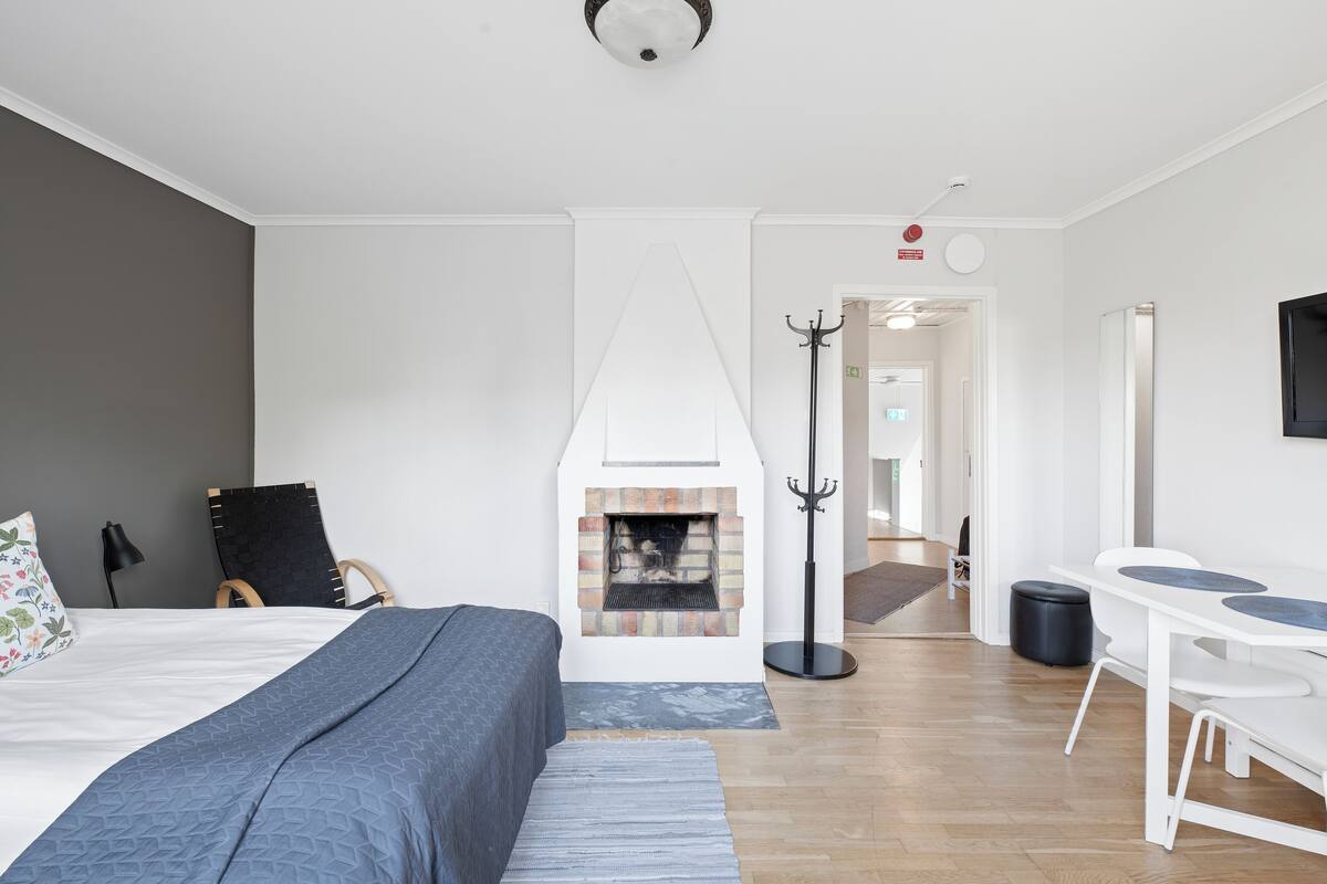 Une chambre moderne avec une cheminée, un lit recouvert d’une couverture bleue, un bureau avec une chaise et un porte-manteau.