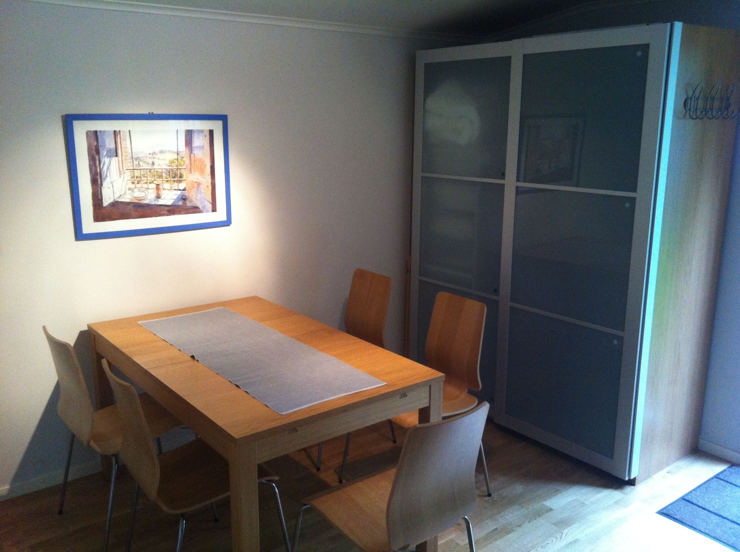 A dining area with a wooden table, four chairs, and a framed picture on the wall.