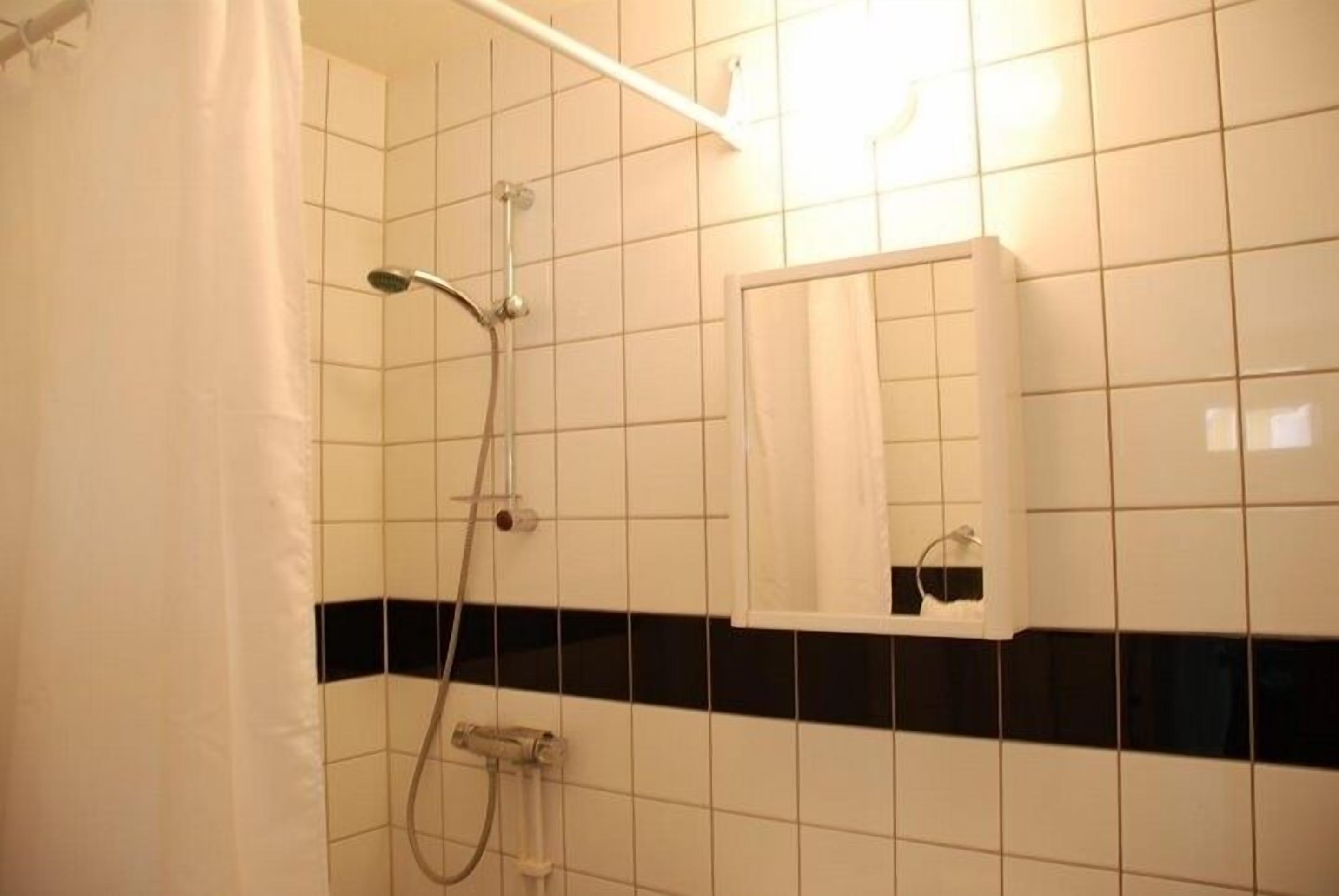 A bathroom with white tiled walls, a black horizontal stripe, a shower with a handheld showerhead, and a white cabinet with a mirror.