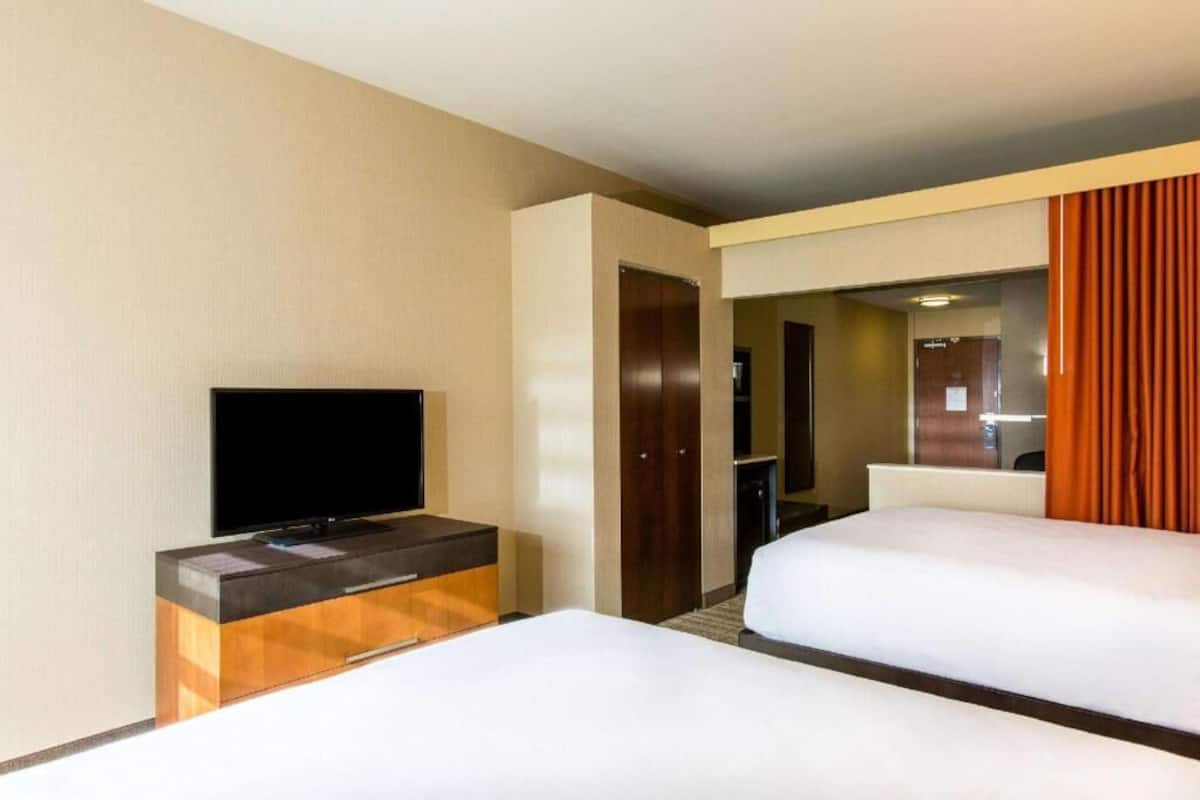 A hotel room with two beds, a flat-screen TV on a wooden console, a door leading to a bathroom, and a mirror.