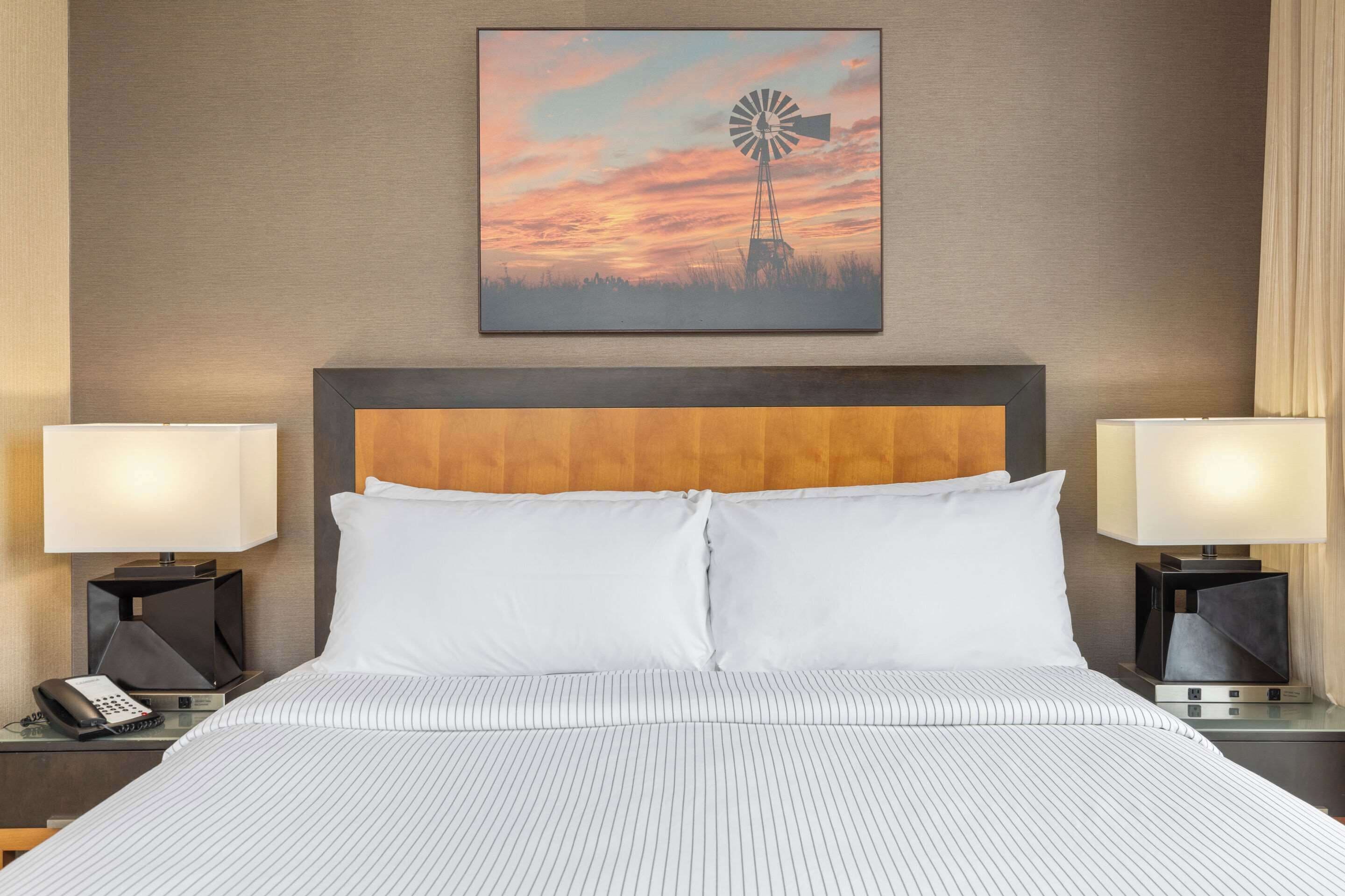 A hotel room with a large bed, two bedside tables with lamps, a wooden headboard, and a wall-mounted picture of a windmill.