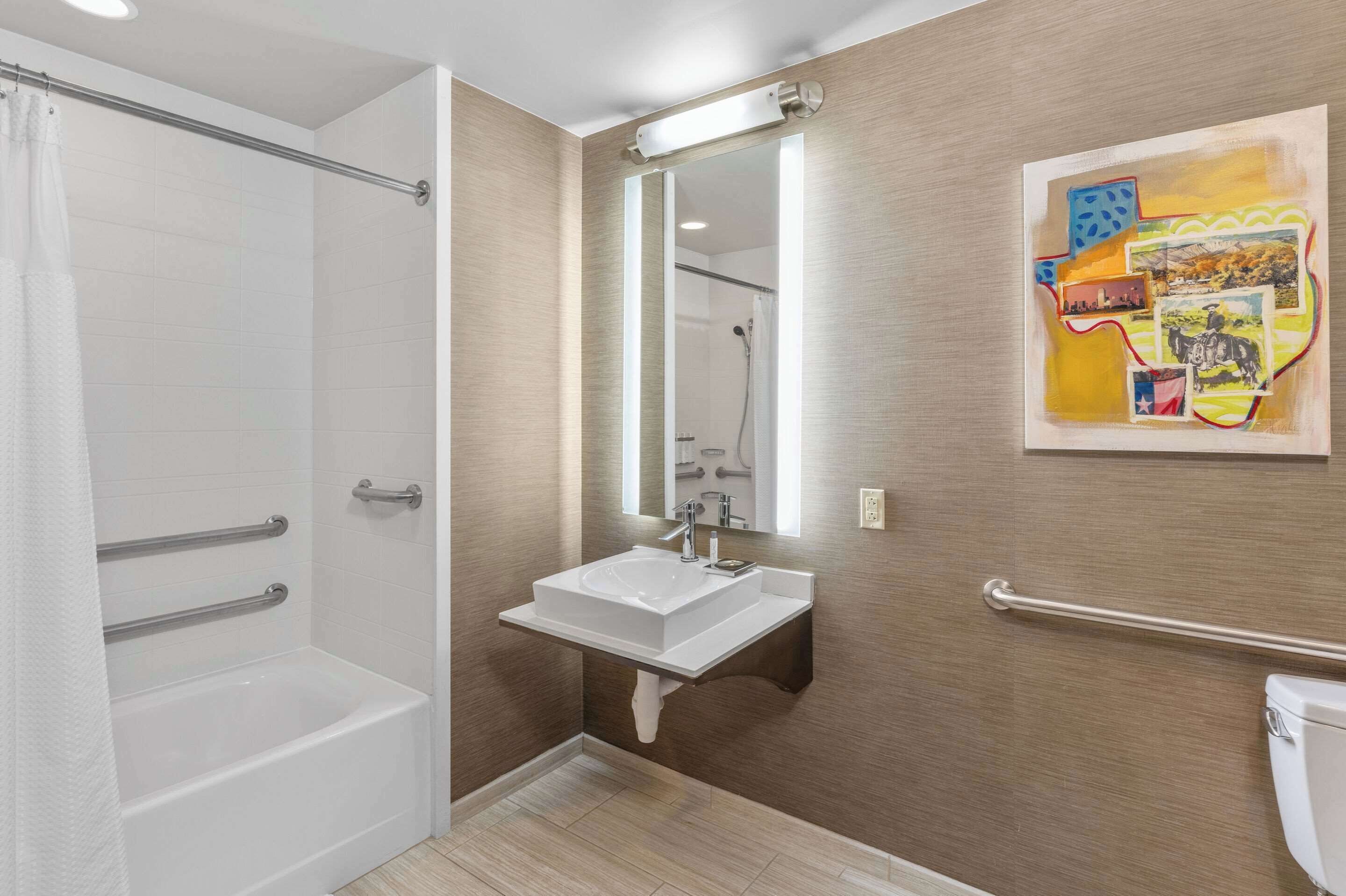 A bathroom with a bathtub, a sink, a mirror, and a handrail.