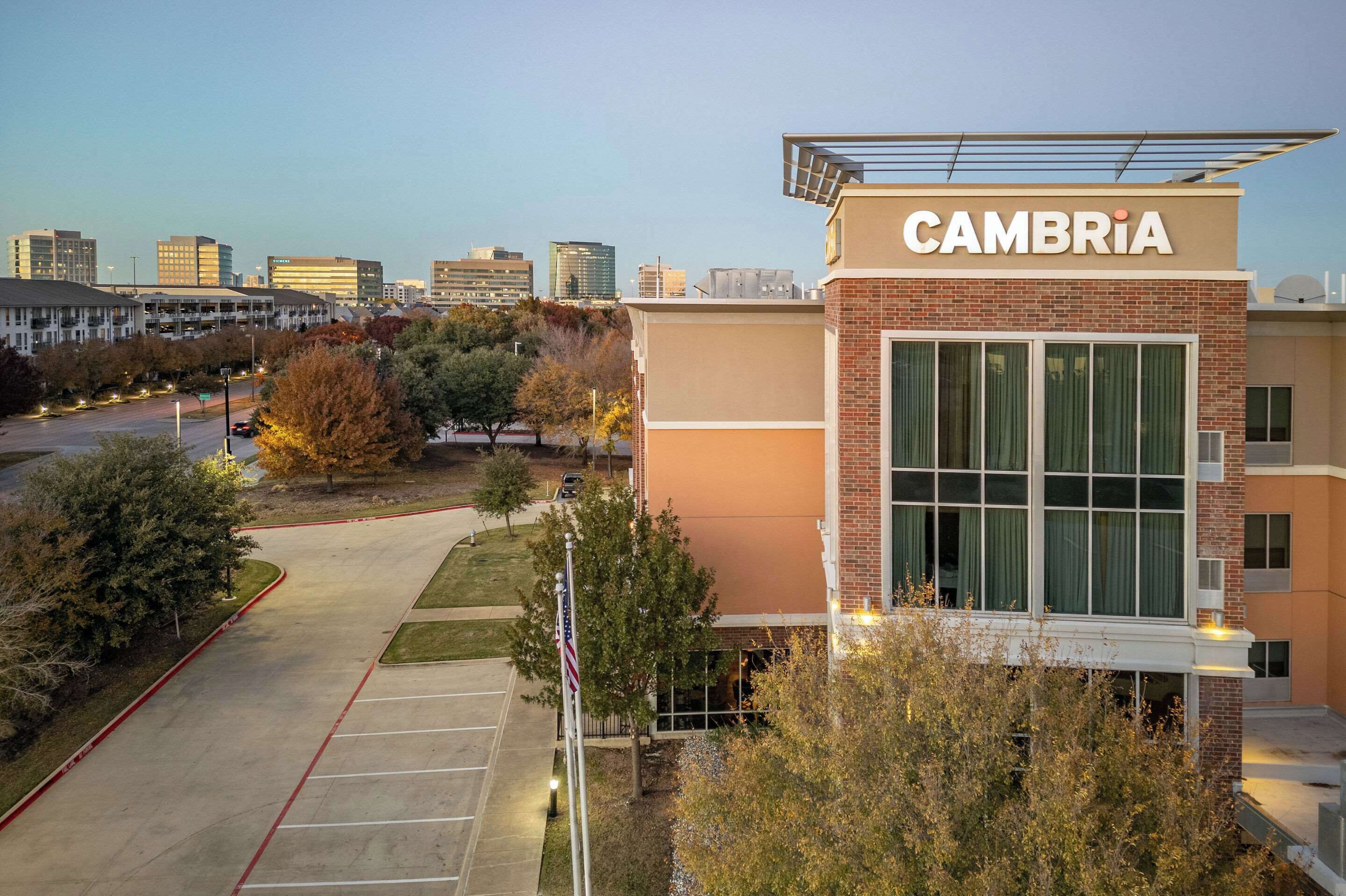 Un edificio moderno con un letrero que dice 'CAMBRIA', rodeado de árboles y un estacionamiento.