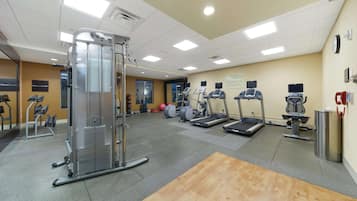 A gym with cardio machines, weight training equipment, and a wooden floor.