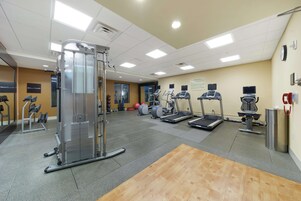 Un gimnasio con máquinas de cardio, equipo de entrenamiento con pesas y suelo de madera.