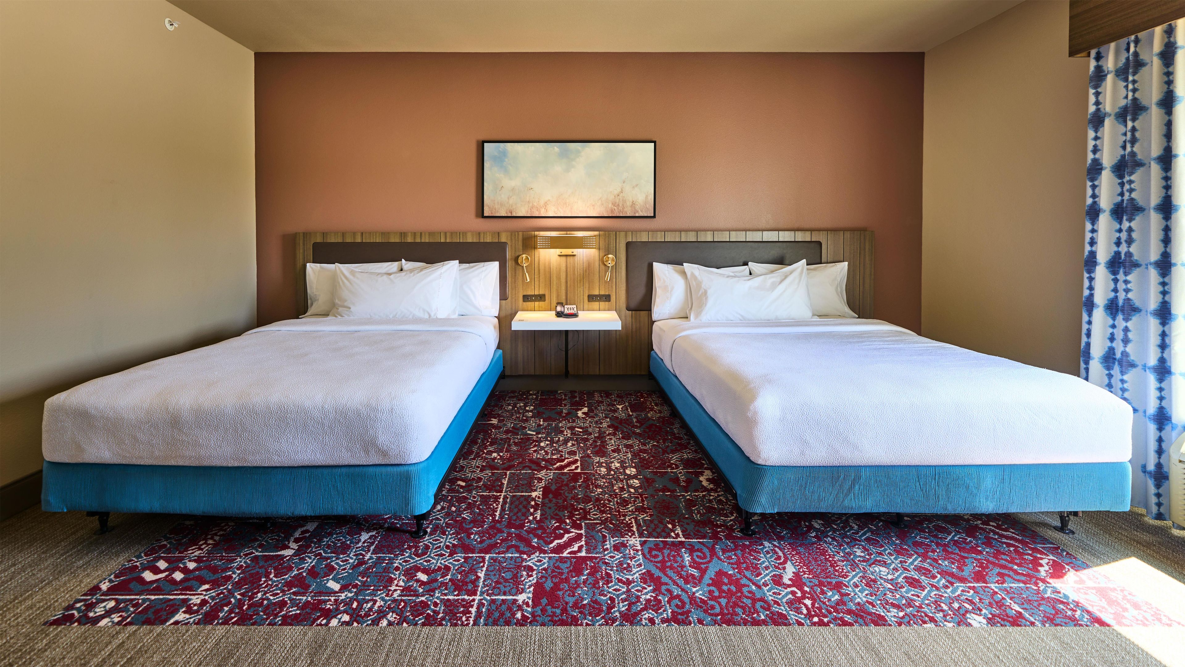 Una habitación de hotel con dos camas, una mesita pequeña y una alfombra estampada.