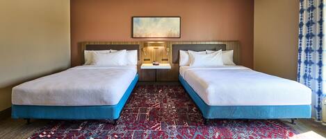 Una habitación de hotel con dos camas, una mesita pequeña y una alfombra estampada.