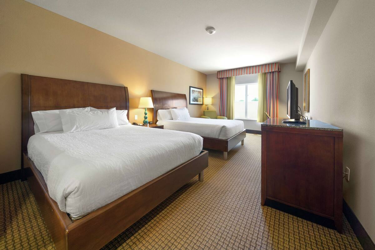 Habitación de hotel con dos camas, cabecera de madera, escritorio con televisor y alfombra estampada.
