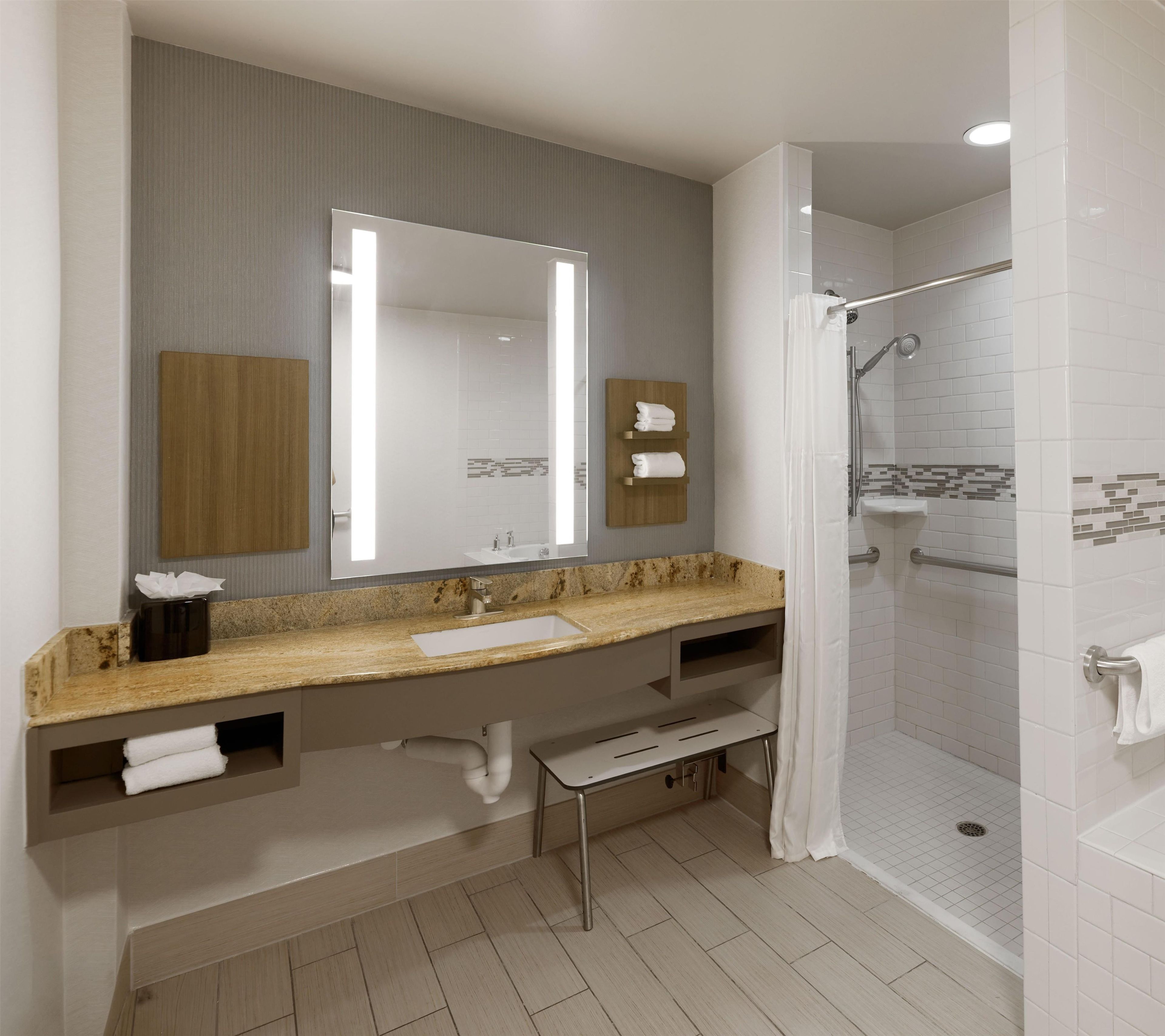 A modern bathroom with a large mirror, a sink, a shower, and a towel rack.