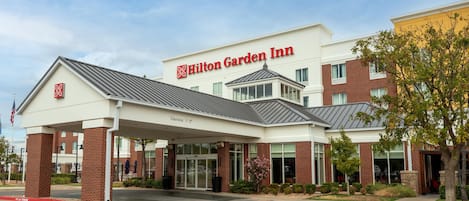 A Hilton Garden Inn with a covered entrance, brick facade, and a clear sky.