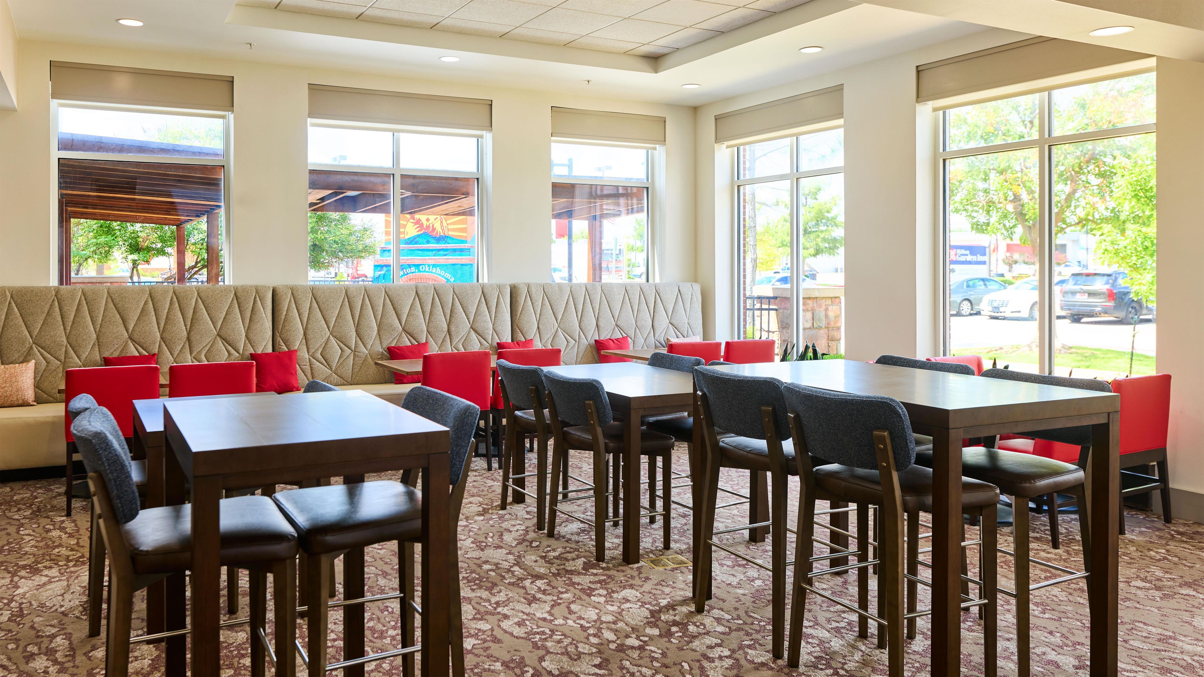 Un interior de restaurante con zona de cabinas, mesas altas y alfombra estampada.