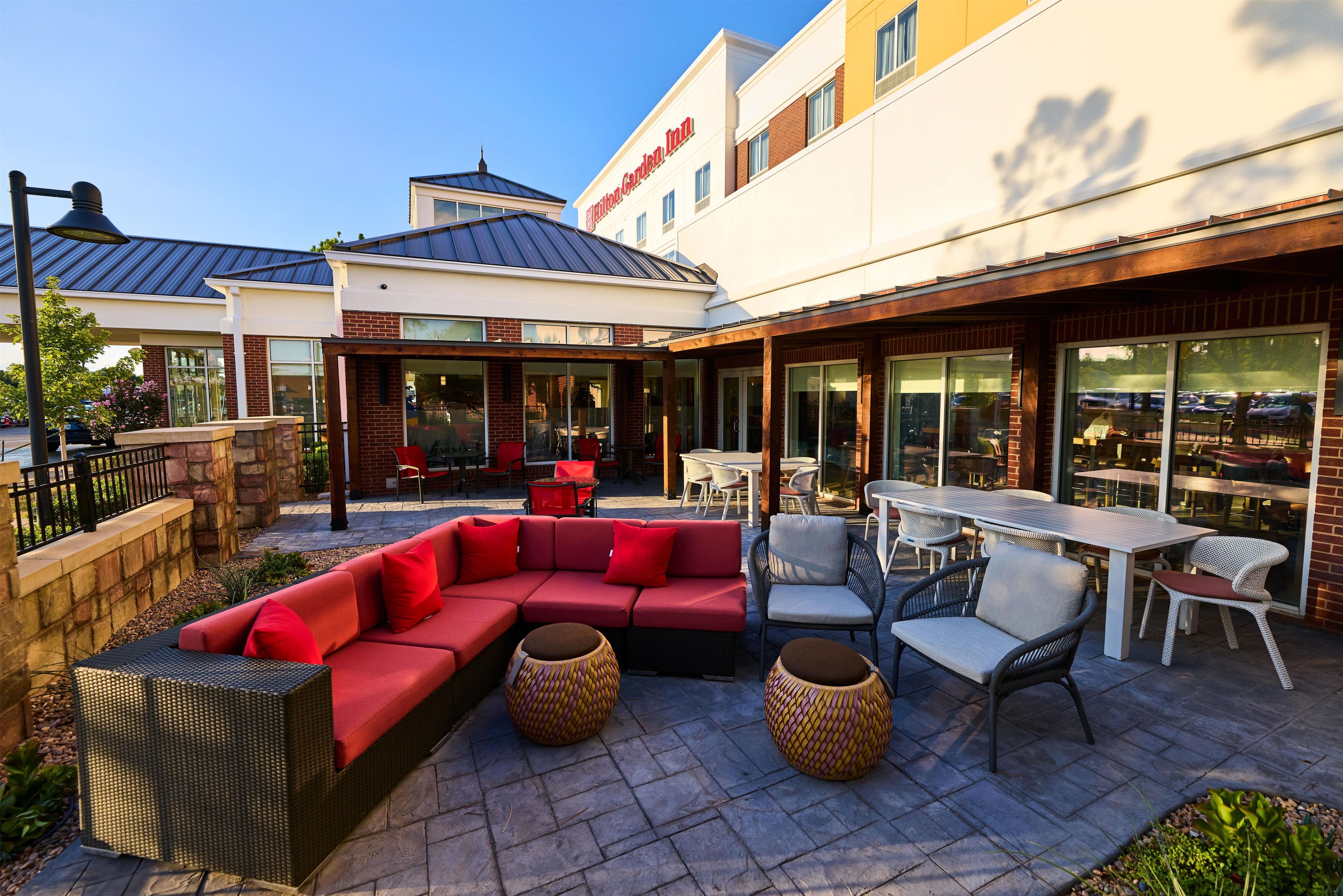 An outdoor patio area with a red sofa, wicker chairs, and a table.