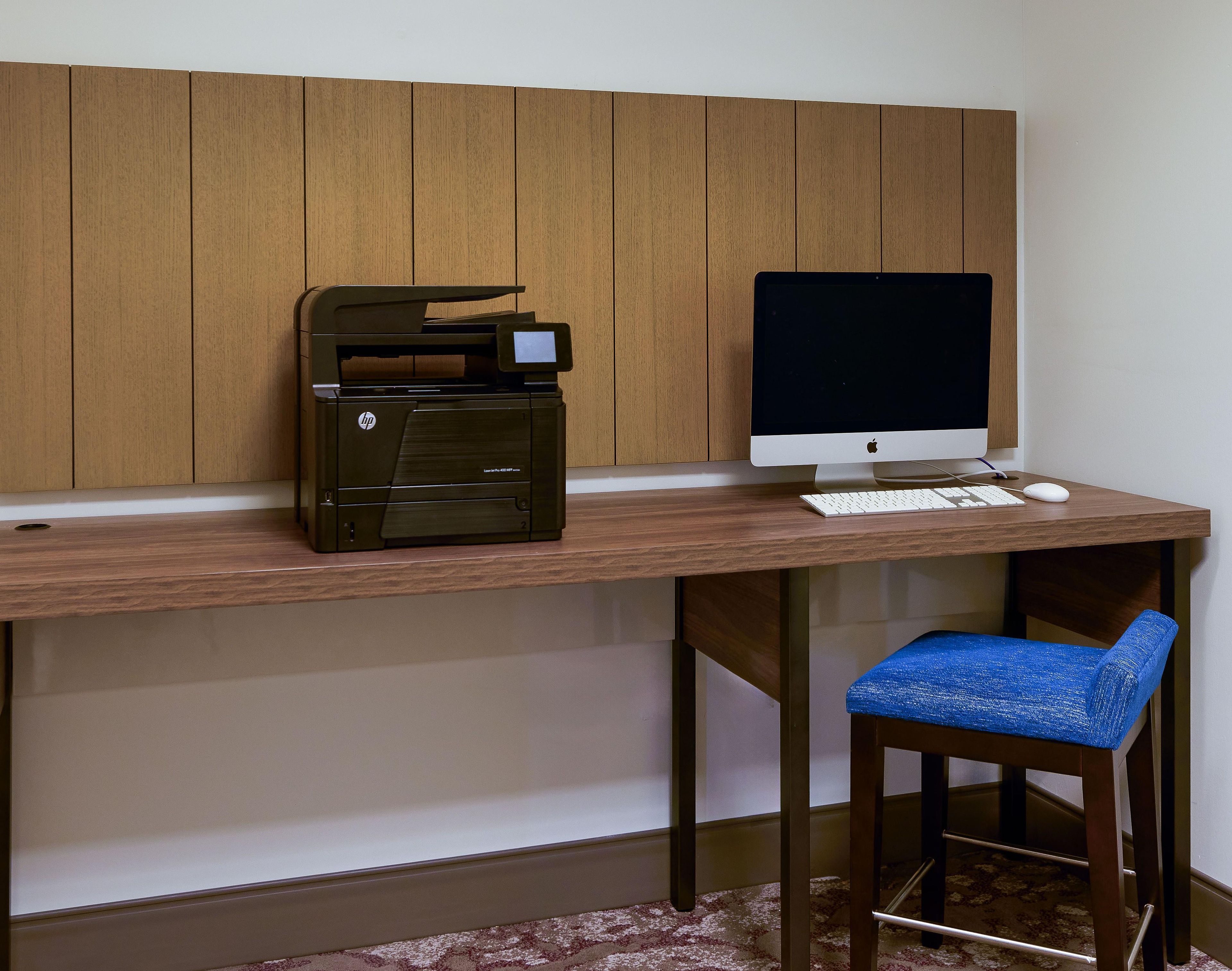 A wooden desk with a printer, a computer monitor, a keyboard, and a blue chair.