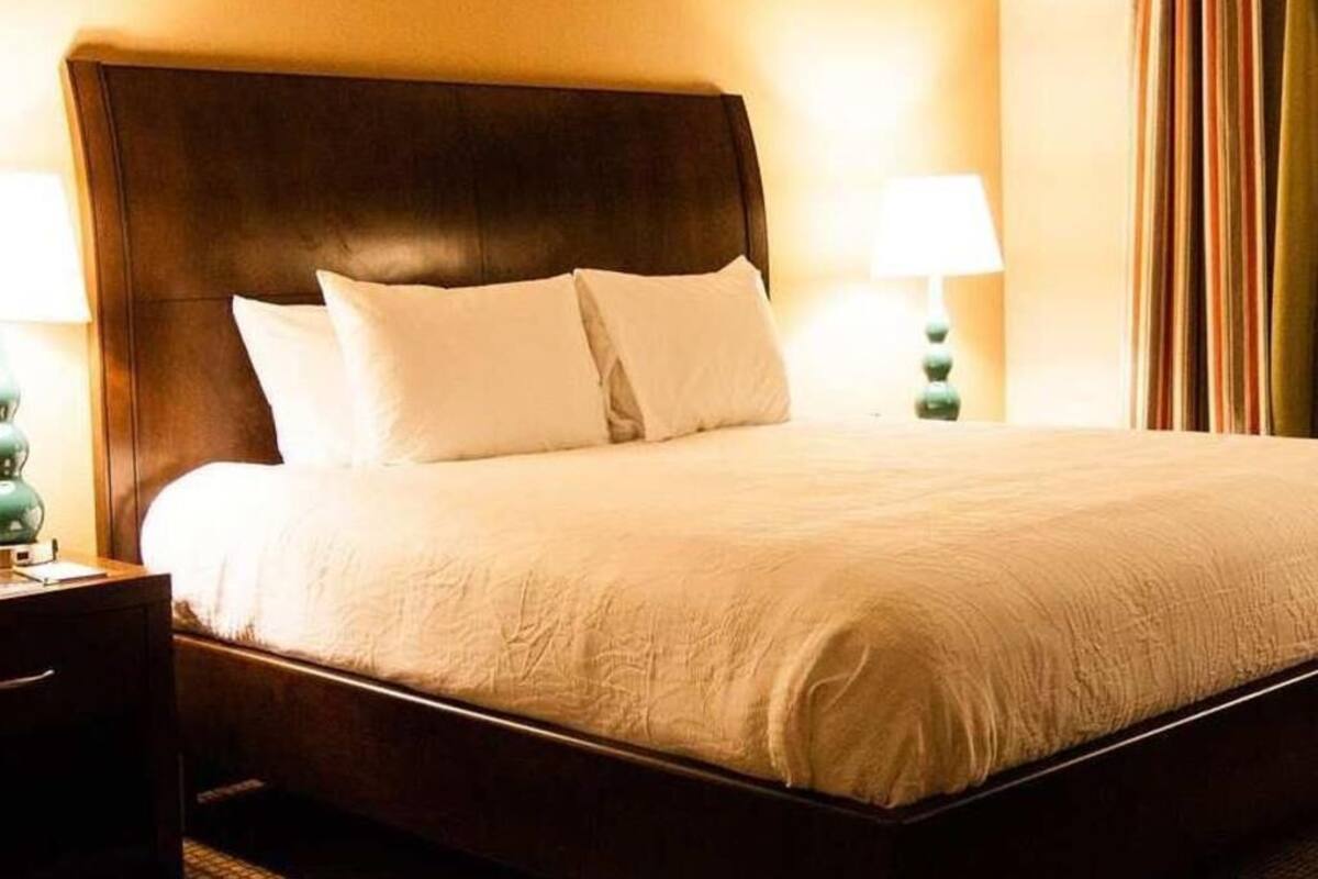 Una habitación de hotel con una cama grande, dos lámparas de noche y una cortina en la ventana.