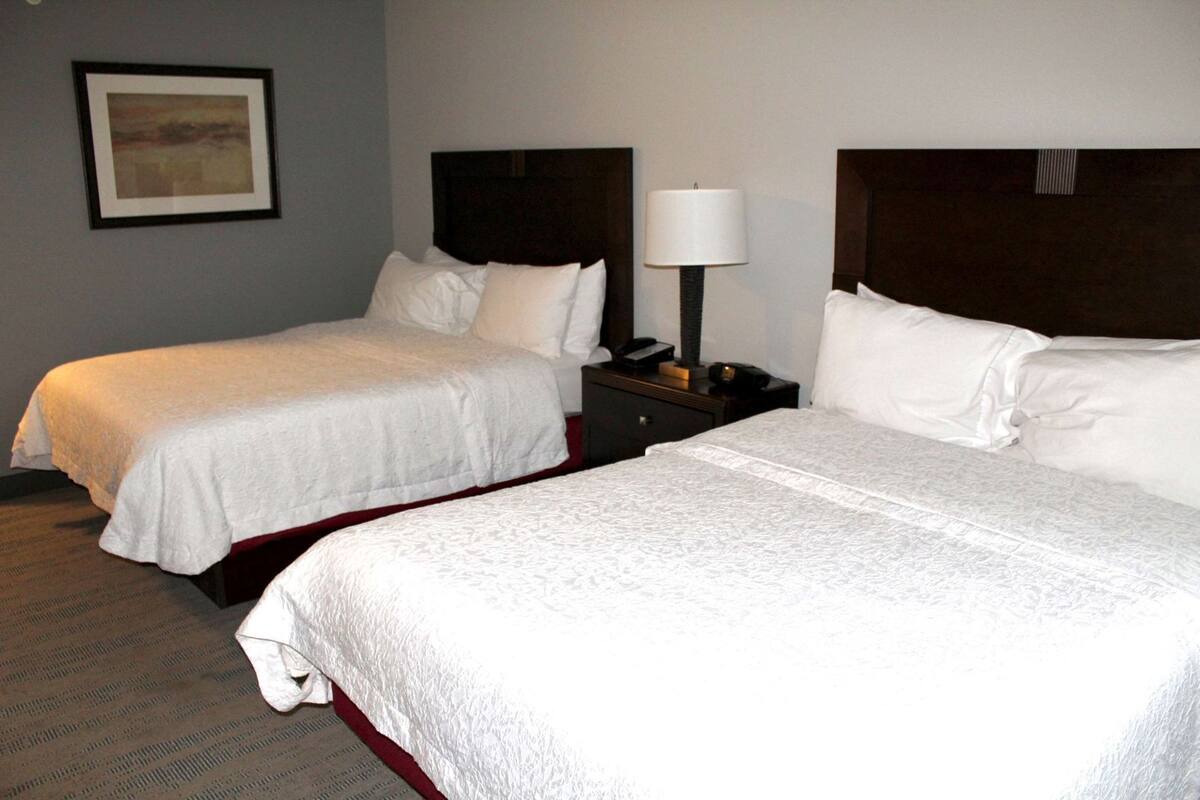 Two single beds with white linens, a nightstand with a lamp, and a framed picture on the wall.
