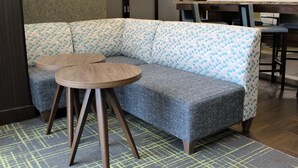 A modern seating area with a grey sofa and two round wooden tables. - Hampton Inn Indianapolis NW/Zionsville (Whitestown)
