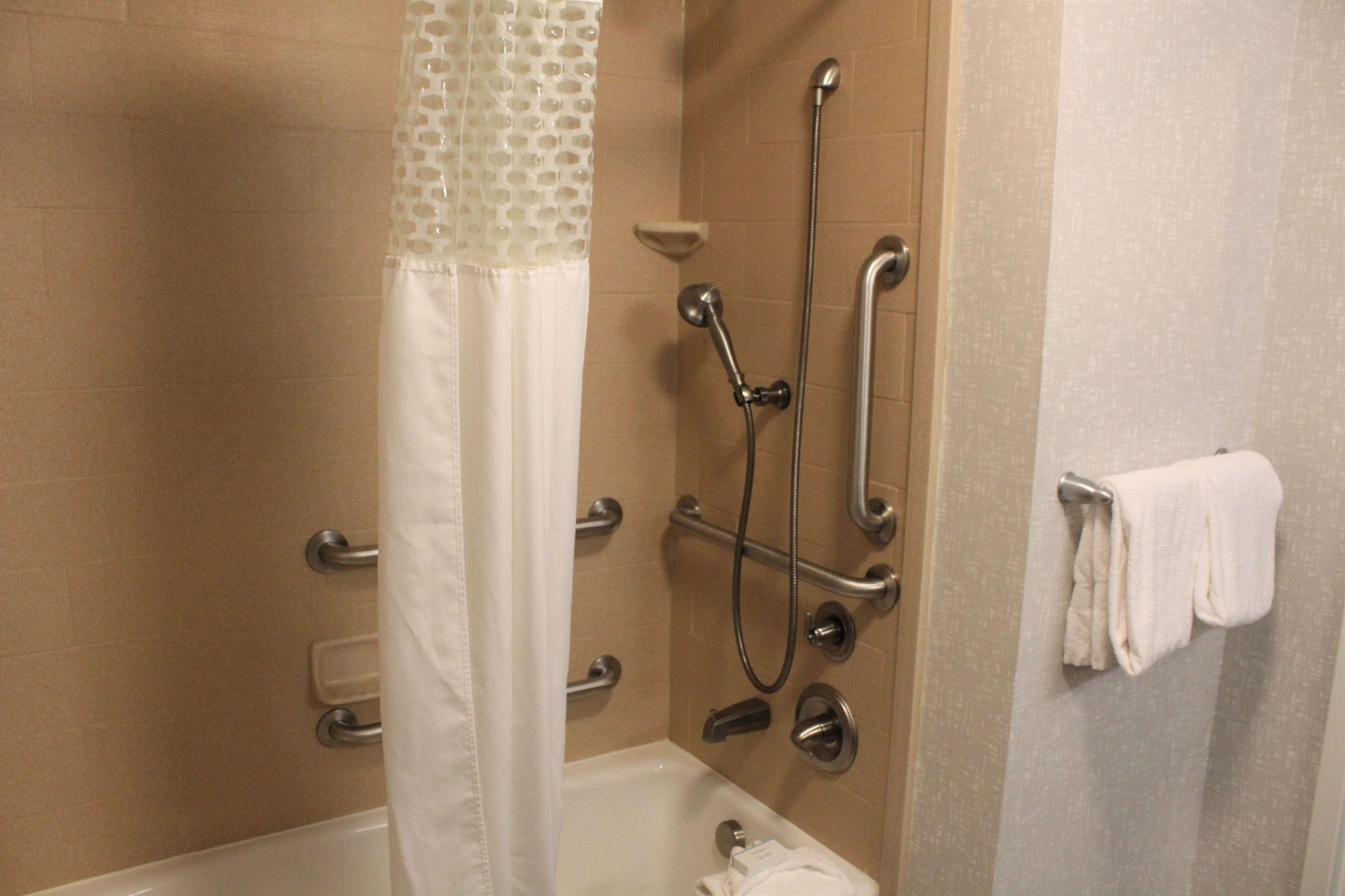 A bathroom with a bathtub, a shower with grab bars, and a towel rack.