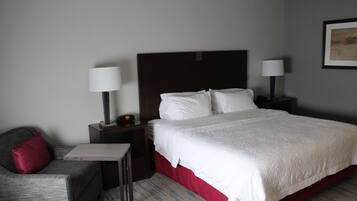 A hotel room with a bed, a nightstand, a lamp, a chair, and a small table.