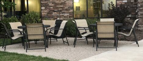 An outdoor seating area with a stone wall and glass doors, featuring a mix of metal and fabric chairs.
