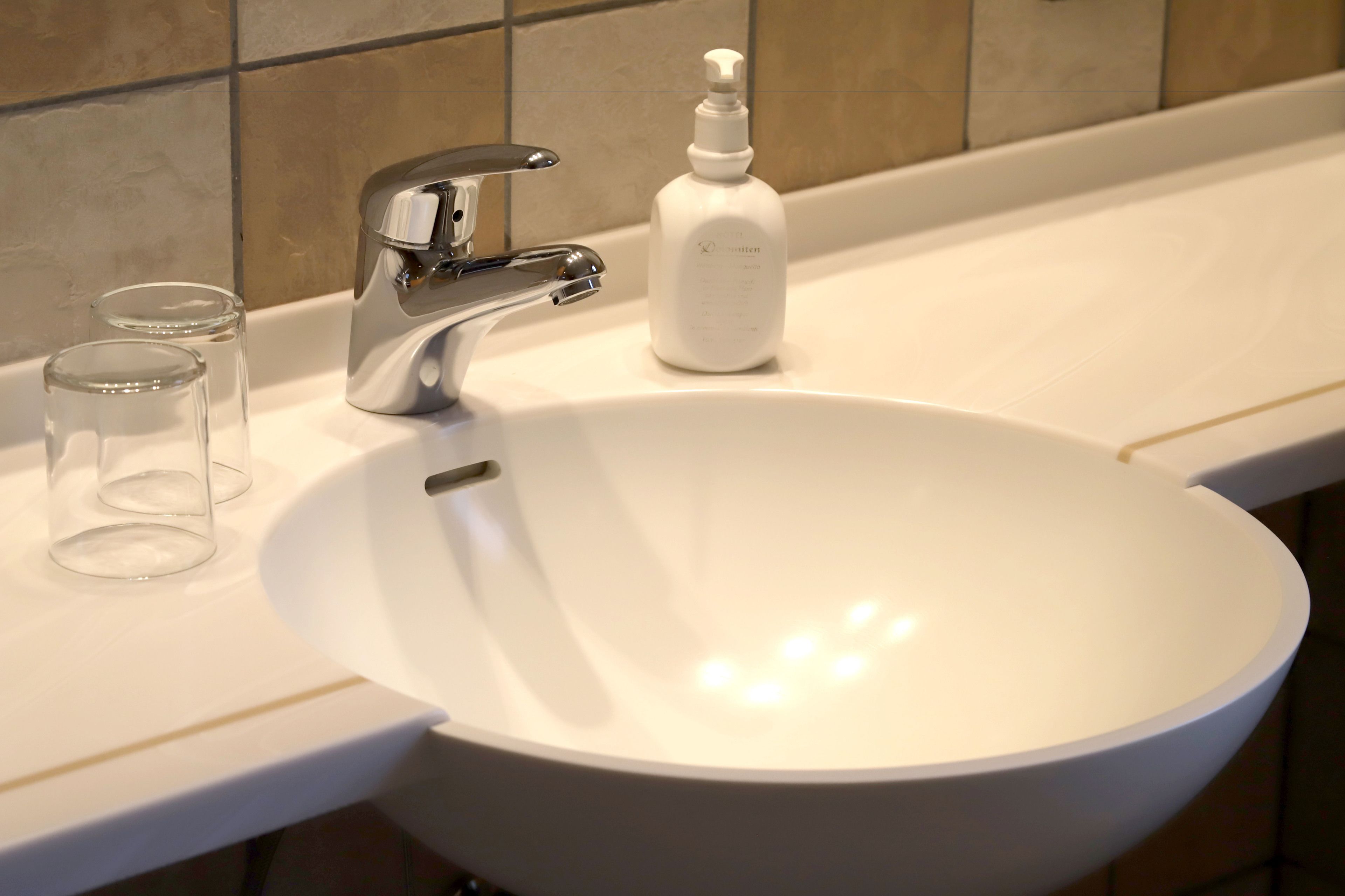 A white bathroom sink with a chrome faucet, a soap dispenser, and two clear glasses on the countertop.